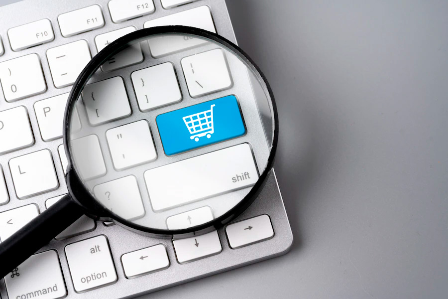 Teclado de computador com lupa sobre um botão azul que contem um ícone de carrinho de compra - Melhor erp Para E-commerce